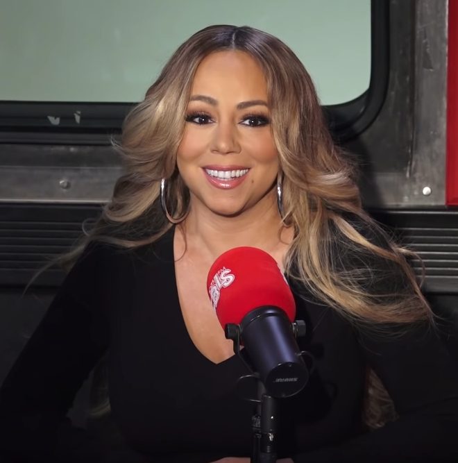 Mariah Carey speaking into a red radio microphone during a 2018 interview
