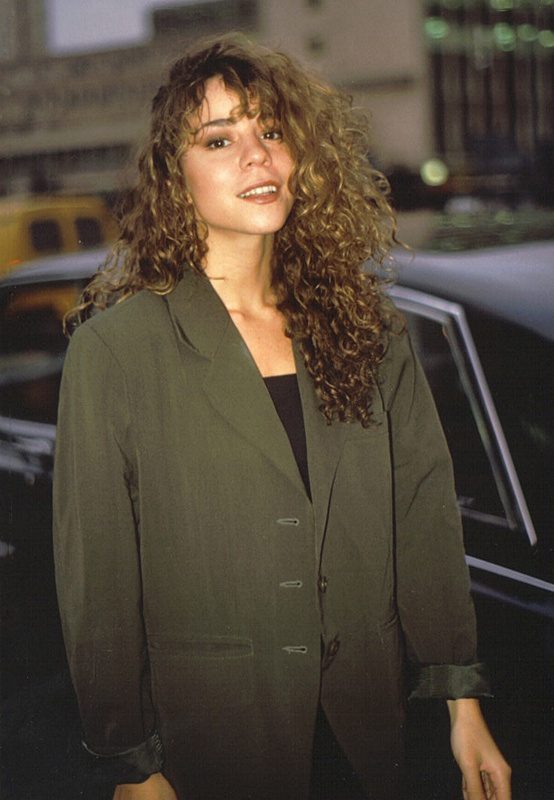 Mariah Carey in a dark oversized jacket walking outside a London theatre in 1990