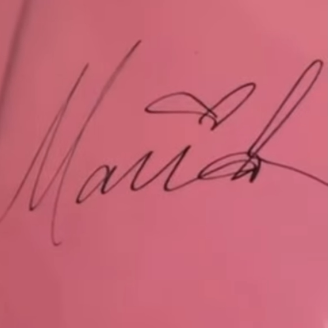 A more open, legible Mariah Carey signature in dark marker on light-colored stock, with a small decorative flourish above it.