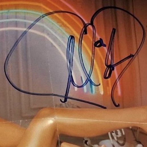 A Mariah Carey signature in dark marker on a photograph whose printed backdrop includes a rainbow motif; a second frame shows a similar example.