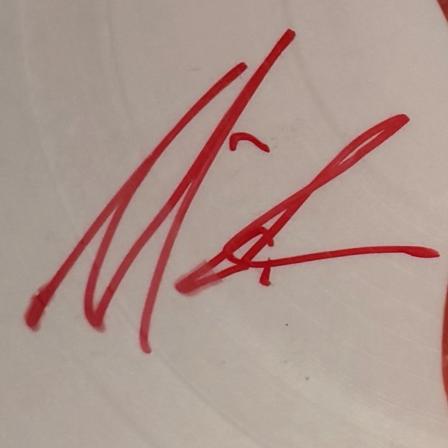 An abbreviated Mariah Carey signature in red marker on the lacquered vinyl surface of a picture disc.